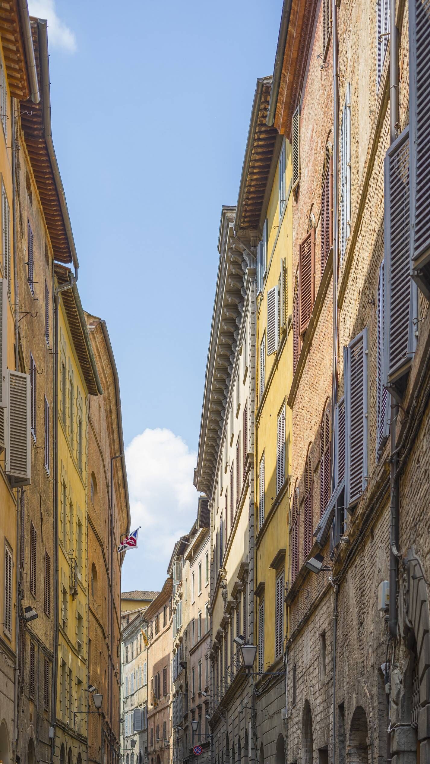 A narrow street flanked by historic buildings with arched windows and shutters.