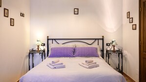 A neatly made bed with a purple pillow and two folded towels, flanked by two bedside tables with lamps, in a room with a simple, clean design. - Farmhouse in Chianti (gaiole in chianti)