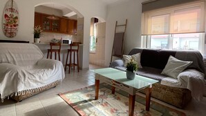 A living room with a sofa, a coffee table, and a dining area with a kitchen in the background.