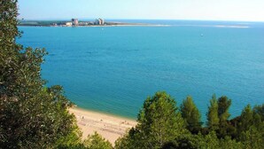 A coastal view with a beach, clear blue water, and a distant cityscape.