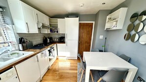 Una cocina moderna con armarios blancos, encimera de madera, horno empotrado y un comedor con mesa y sillas.