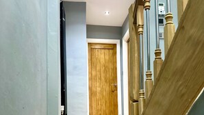 Una escalera de madera con peldaños que conducen a una habitación con una puerta de madera y un interruptor de luz en la pared.