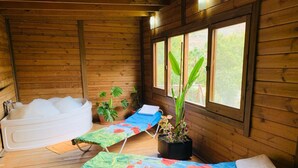 Una baita in legno con una vasca da bagno, due lettini prendisole e piante in vaso.