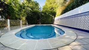 Una piscina rettangolare con bordo piastrellato, circondata da un solarium in pietra e un muro decorativo con motivo blu e bianco.