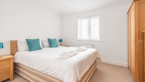 Un dormitorio con cama, mesita de noche, lámpara, ventana con persianas y armario.