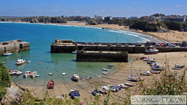 Un pueblo costero con un puerto deportivo, playa de arena y un acantilado rocoso.