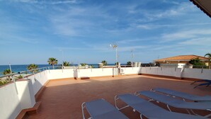 Una terraza en la azotea con sillones blancos, vistas al mar y suelo de baldosas.