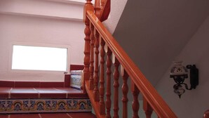 Una escalera de madera con balaustres y peldaños estampados en rojo que conduce a un rellano con un ventanal.