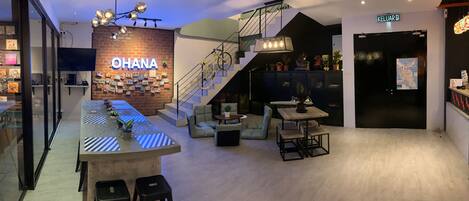 Una moderna hall d'albergo con zona bar, posti a sedere, una scala e un cartello con scritto "OHANA".