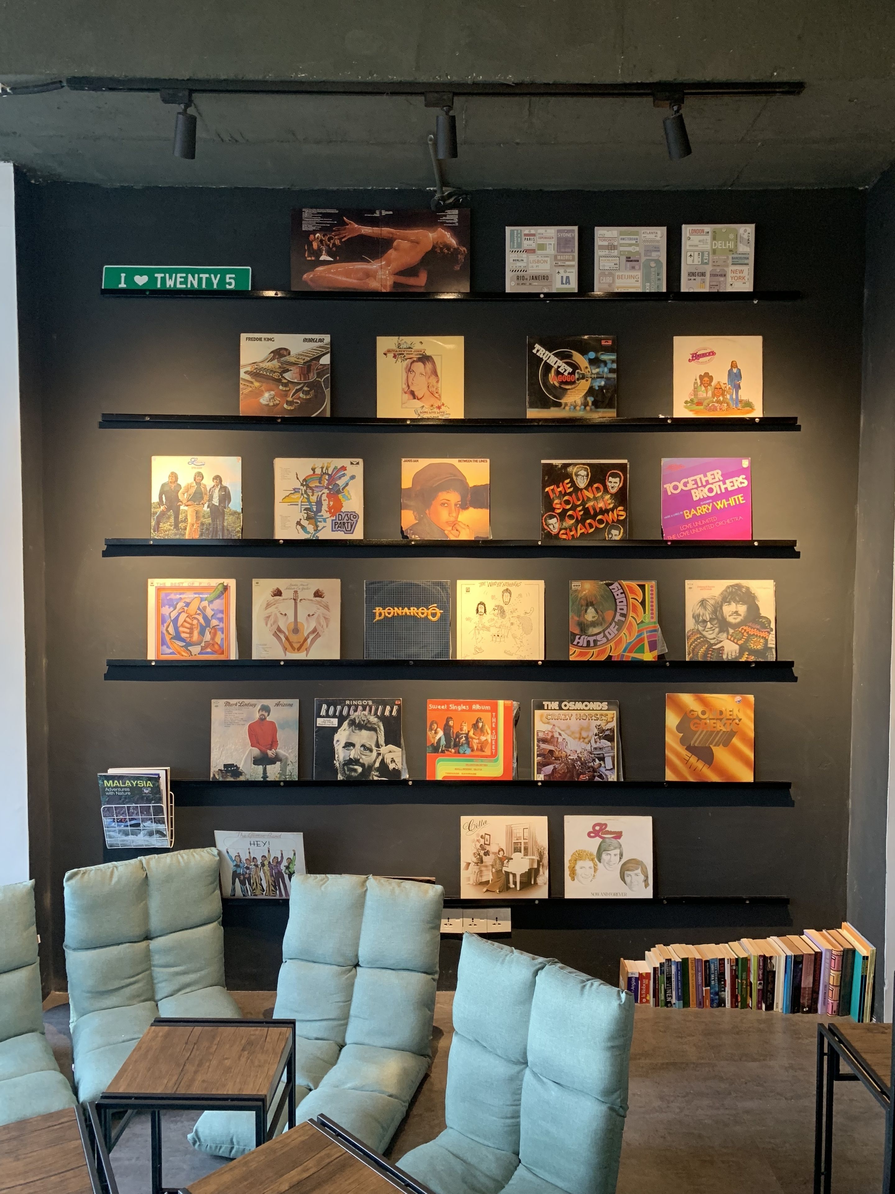 A wall with multiple shelves displaying various album covers. There are several cushioned chairs and a small table in the foreground.