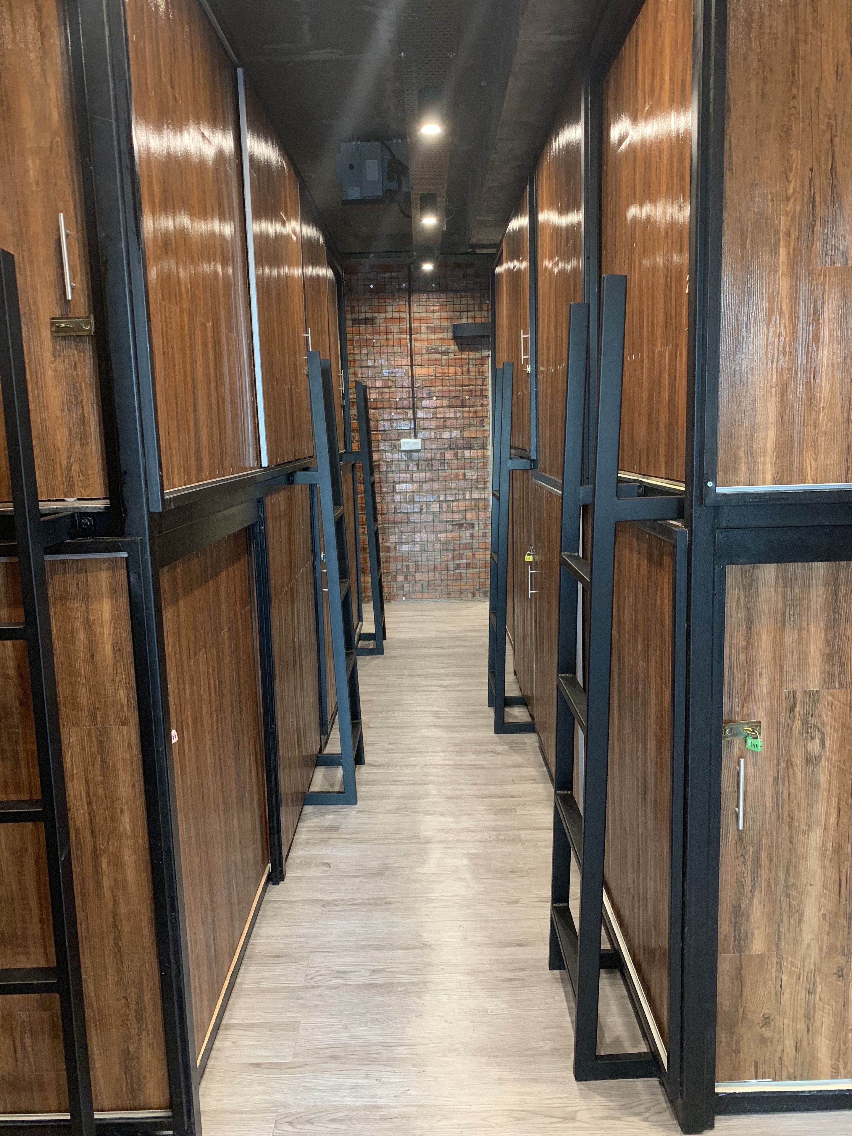 A row of wooden lockers with metal frames, a brick wall in the background, and a wooden floor.