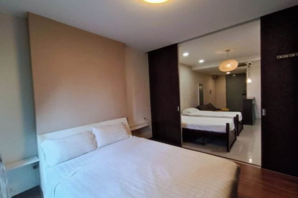 Une chambre à coucher avec un grand lit, une armoire et un miroir qui reflète une autre pièce où se trouvent un lit et un bureau.