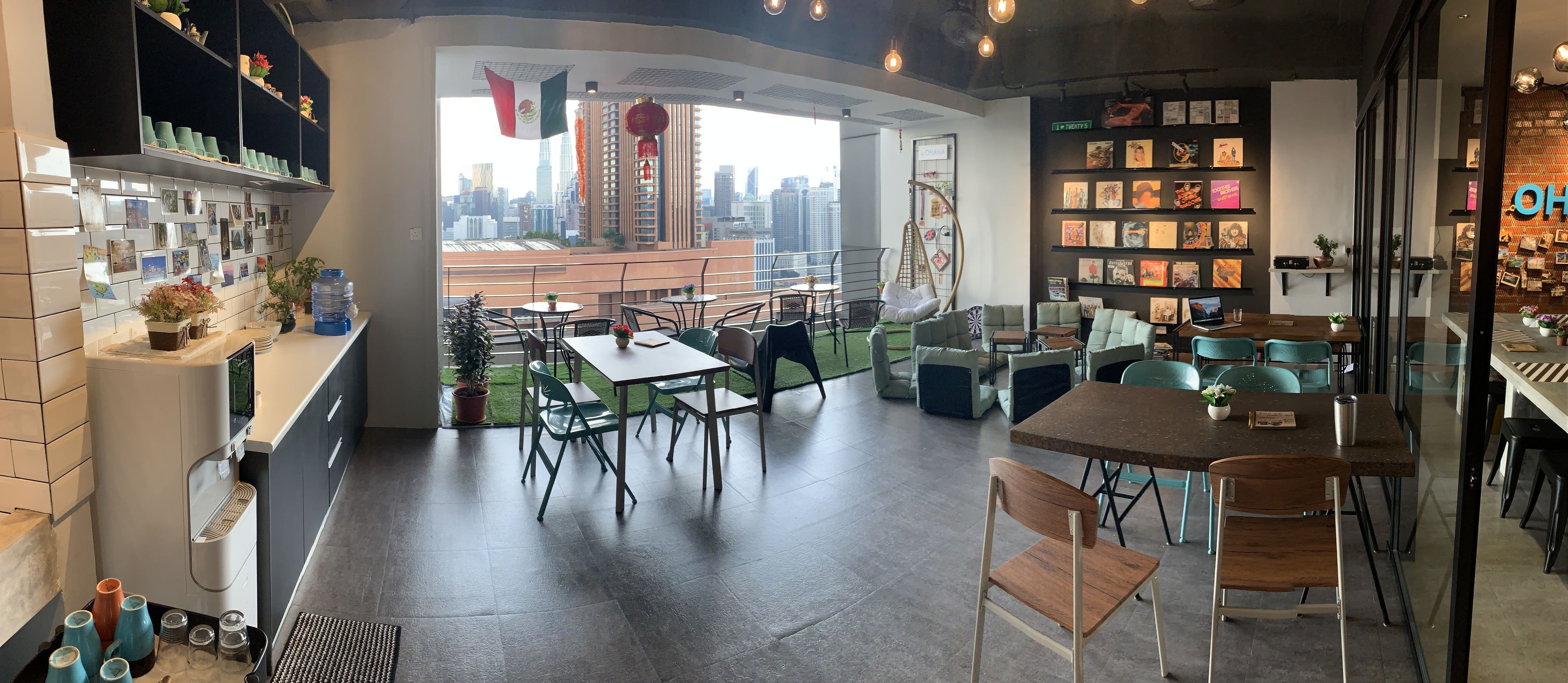 A modern cafe with a city view, featuring a mix of seating arrangements and a wall adorned with books and decorations.