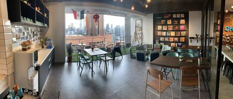 A modern cafe with a city view, featuring a mix of seating arrangements and a wall adorned with books and decorations.