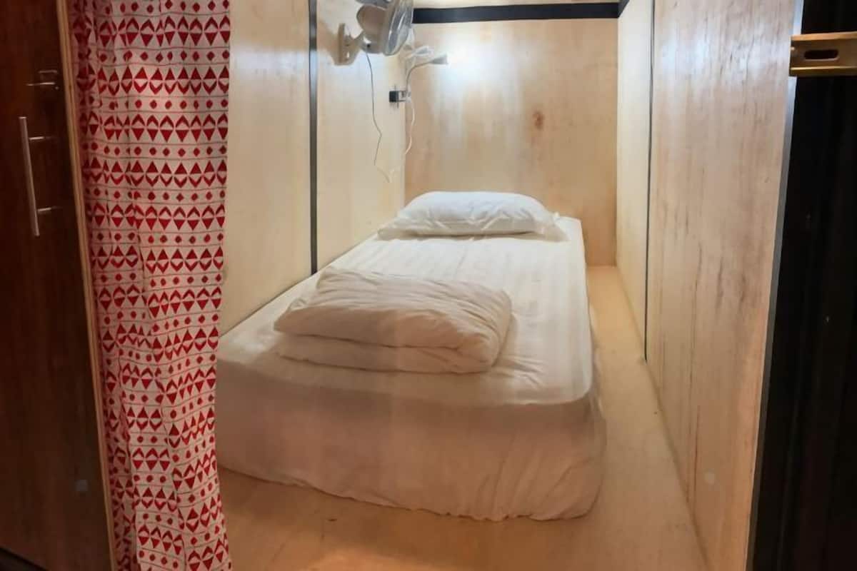 Une petite chambre avec un lit simple, un plancher en bois, un lit blanc et un rideau à motifs.
