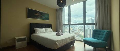 A modern bedroom with a large bed, a blue armchair, and a city view through large windows.