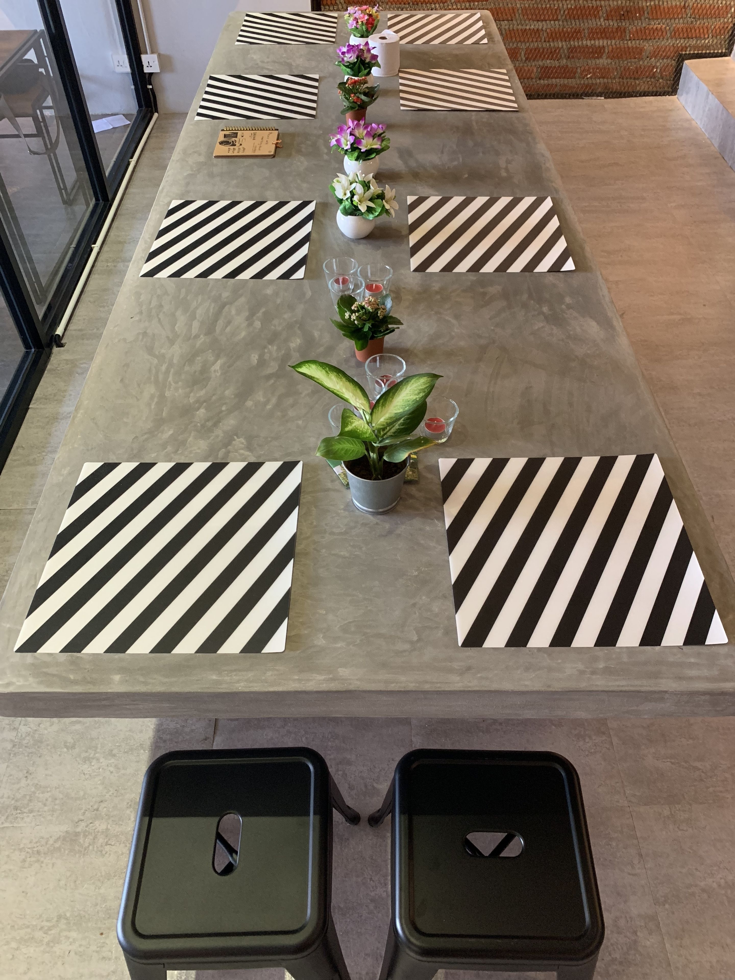 Una mesa larga y estrecha con individuales a rayas blancas y negras, plantas en macetas y velas.