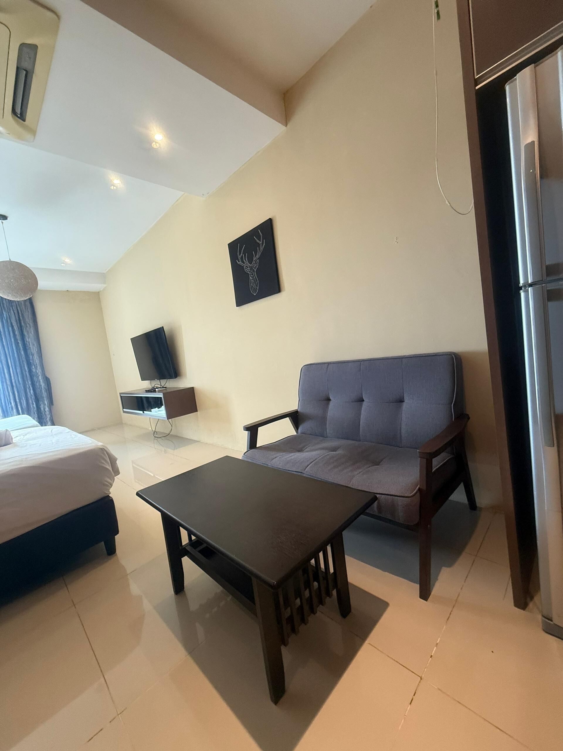 A modern hotel room with a bed, a sofa, a small table, a flat-screen TV, and a refrigerator.