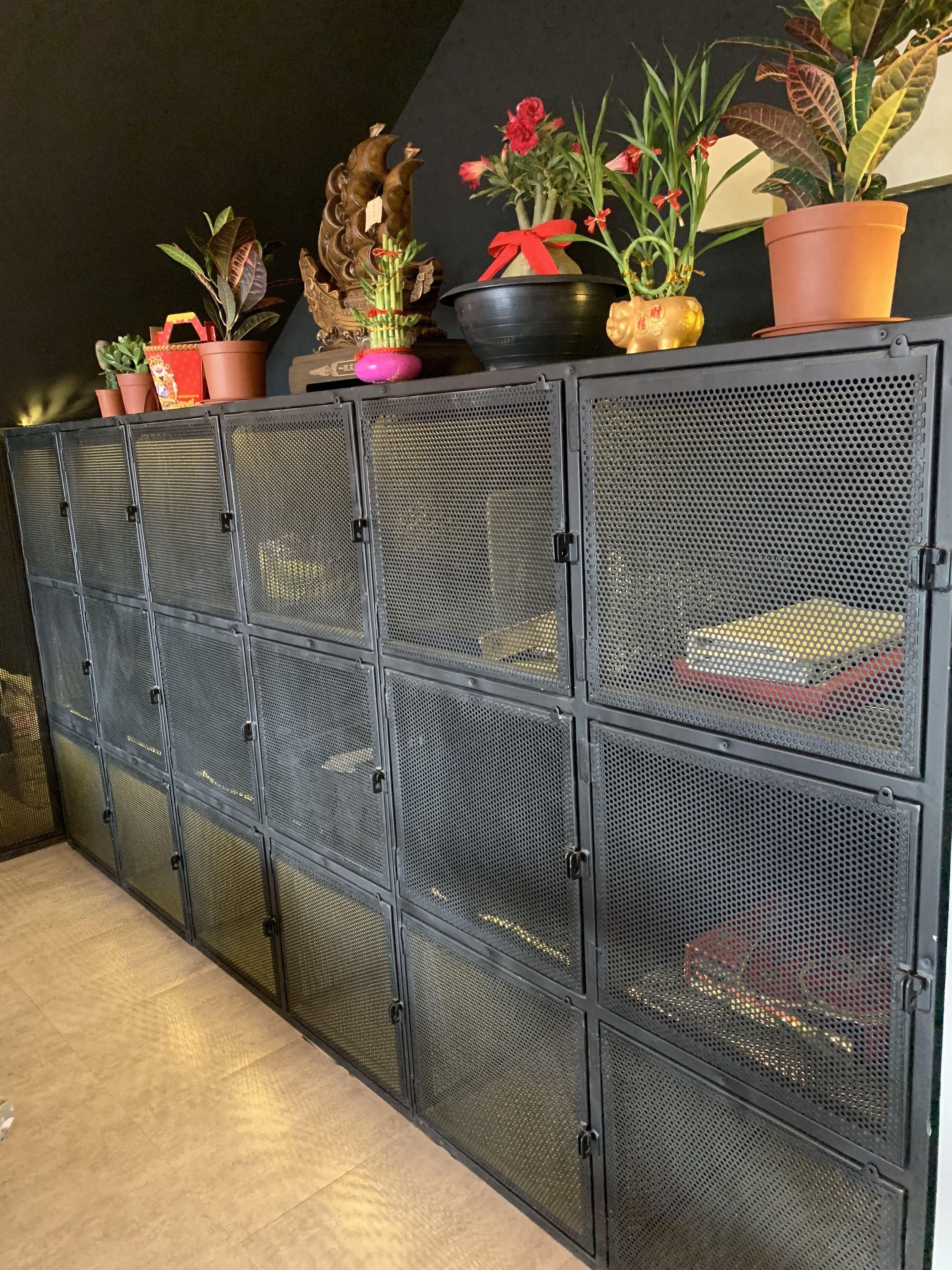 Un meuble de rangement en métal, doté de plusieurs compartiments, dont certains contiennent des plantes en pot et des objets décoratifs.