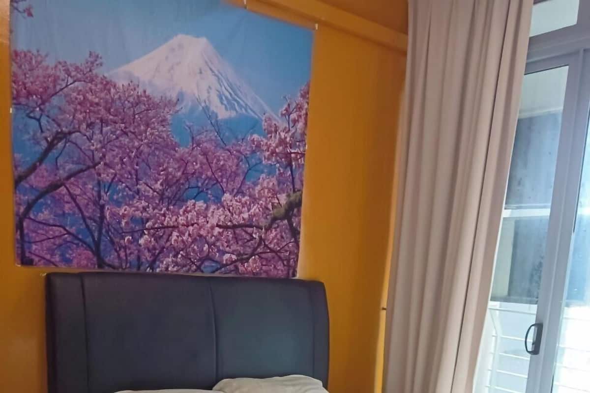 Un lit bien fait, recouvert de draps blancs, dans une pièce où un grand tableau représentant une montagne et des fleurs de cerisier orne le mur.