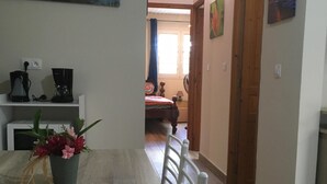 A dining area with a wooden table, chairs, and a potted plant. There is a kitchen area with appliances visible in the background. - Beautiful T3 in tropical forest with swimming pool (saint joseph)