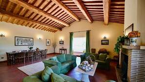 A spacious living room with green sofas, a dining area with wooden furniture, and a fireplace. - Tenuta Santa Cristina - Luxury 8 beds Villa w/ private Pool and Tennis near Rome (Lazio)