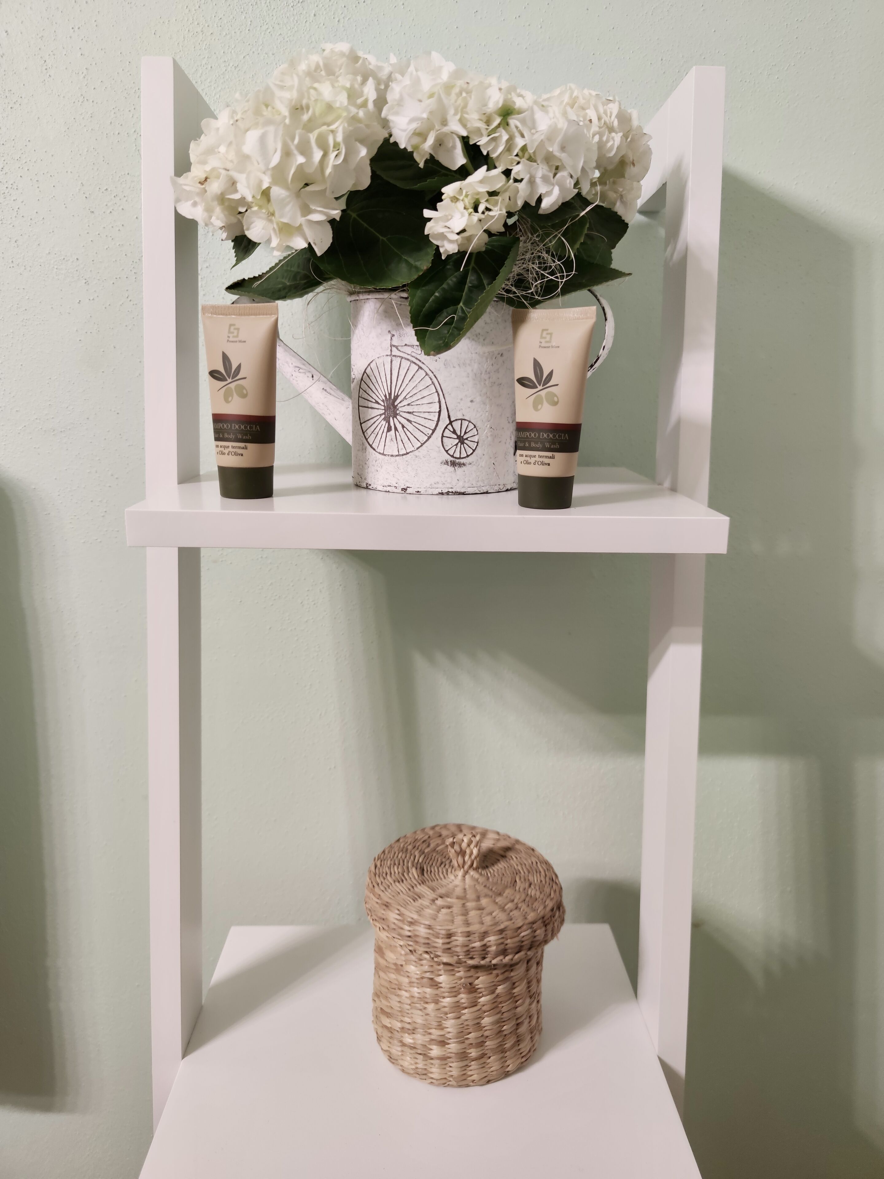 A shelf with a white vase containing white flowers, two skincare products, and a woven basket.