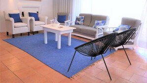 Un saló modern amb una catifes blava, mobles blancs i una finestra gran amb cortines blanques.