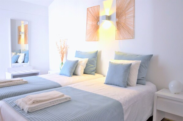 A hotel room with two beds, a nightstand, a mirror, and wall-mounted sconces.