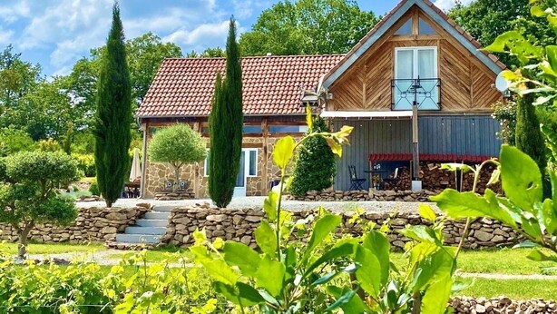 Una casa de dos pisos con techo de tejas rojas, un porche de madera y un muro de piedra.