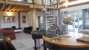Una cocina moderna con una isla central, una escalera de caracol y un comedor con sofá rojo y sillas negras.
