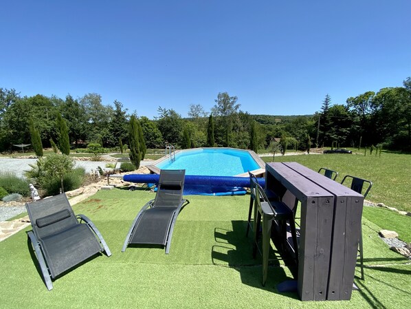 En baghave med swimmingpool, to liggestole, et træbord og en grill.