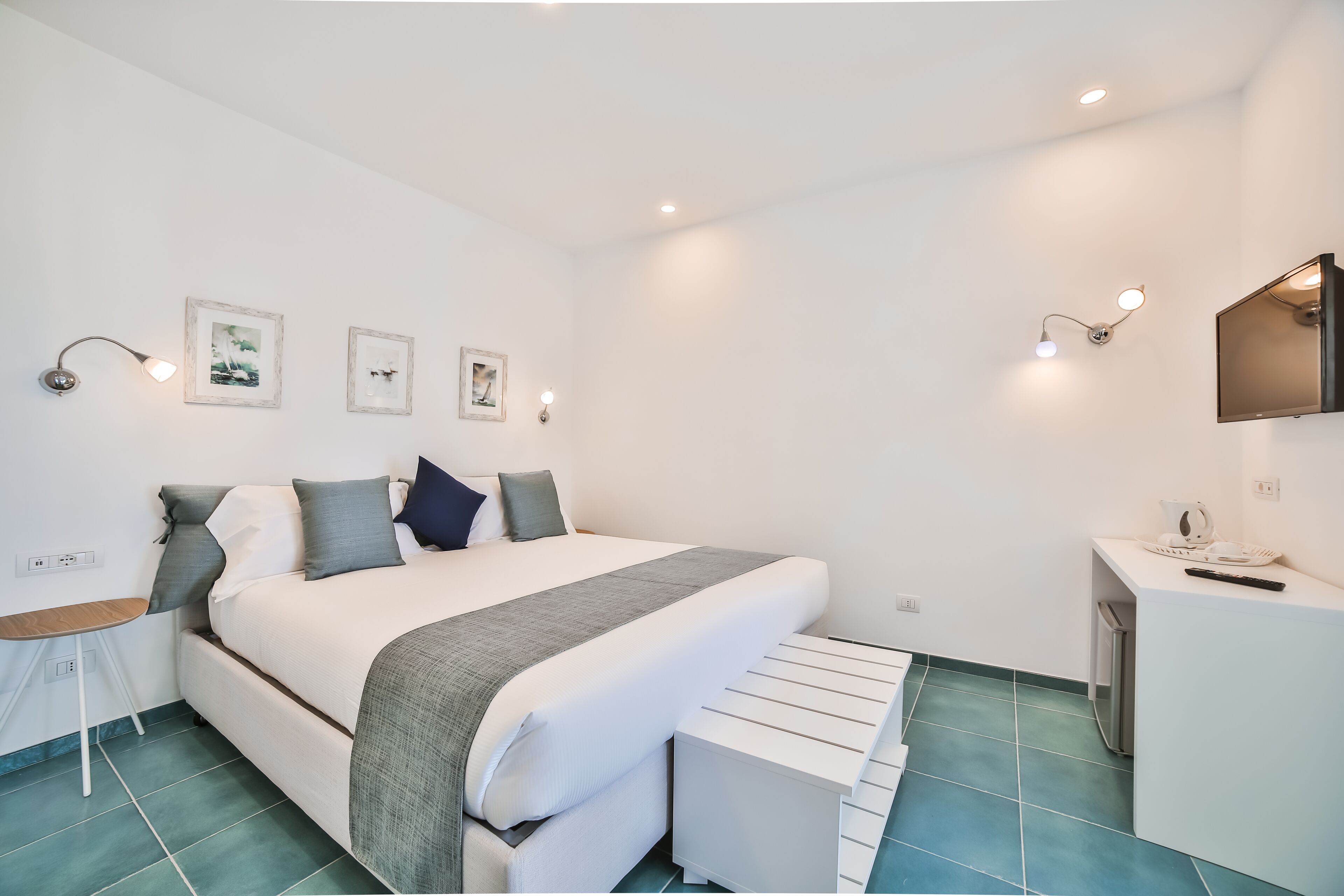 A modern bedroom with a bed, bedside tables, a small desk, and wall-mounted lights.