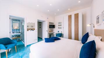 A modern hotel room with a large bed, a blue chair, a vanity with a mirror, and a television.