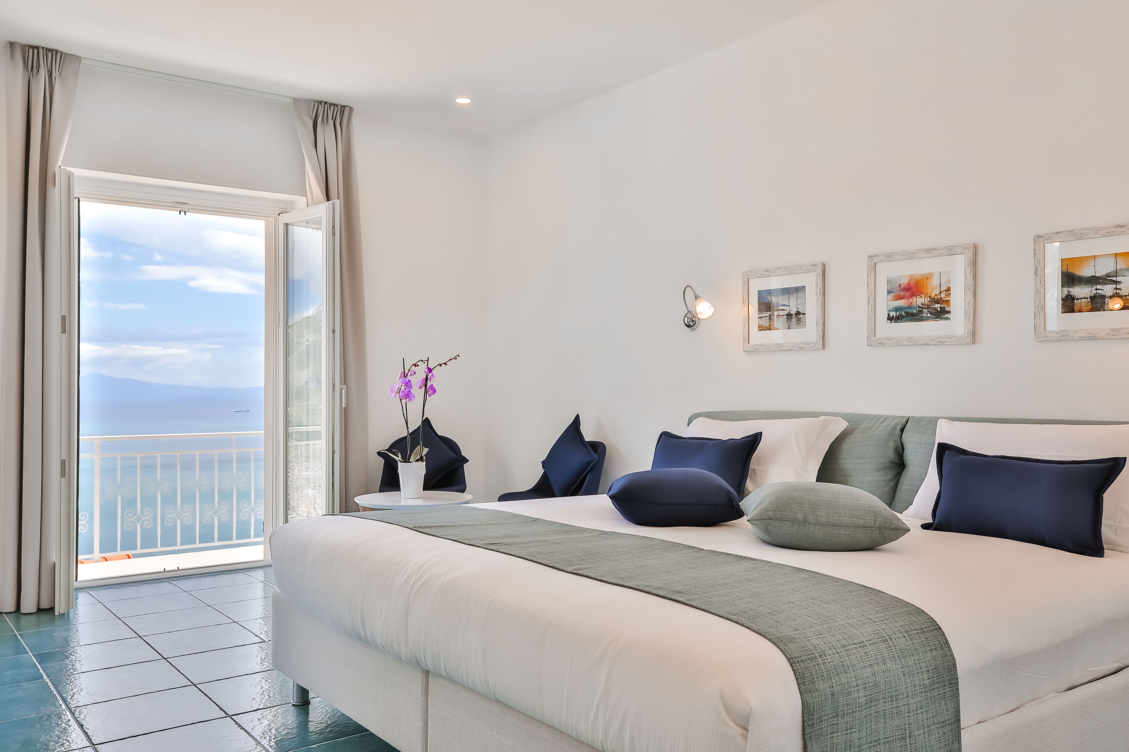 Een hotelkamer met een groot bed, een balkon met uitzicht en drie ingelijste foto’s aan de muur.