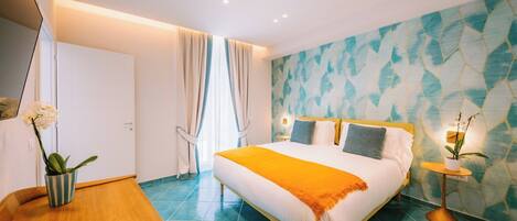 Quarto de hotel moderno com uma cama grande, uma mesinha de madeira, uma pequena mesa redonda com uma planta e um banheiro com porta branca.