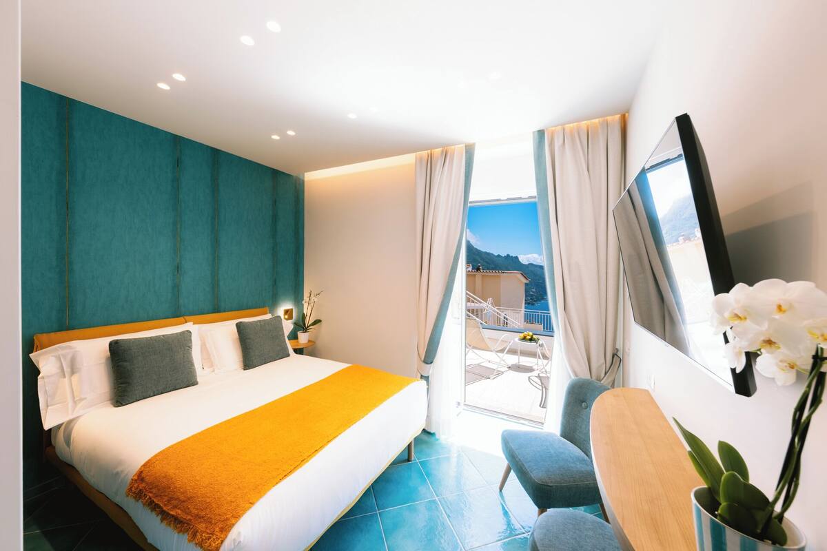 Una camera d'albergo moderna con un letto grande, un balcone vista mare e una scrivania con una sedia.