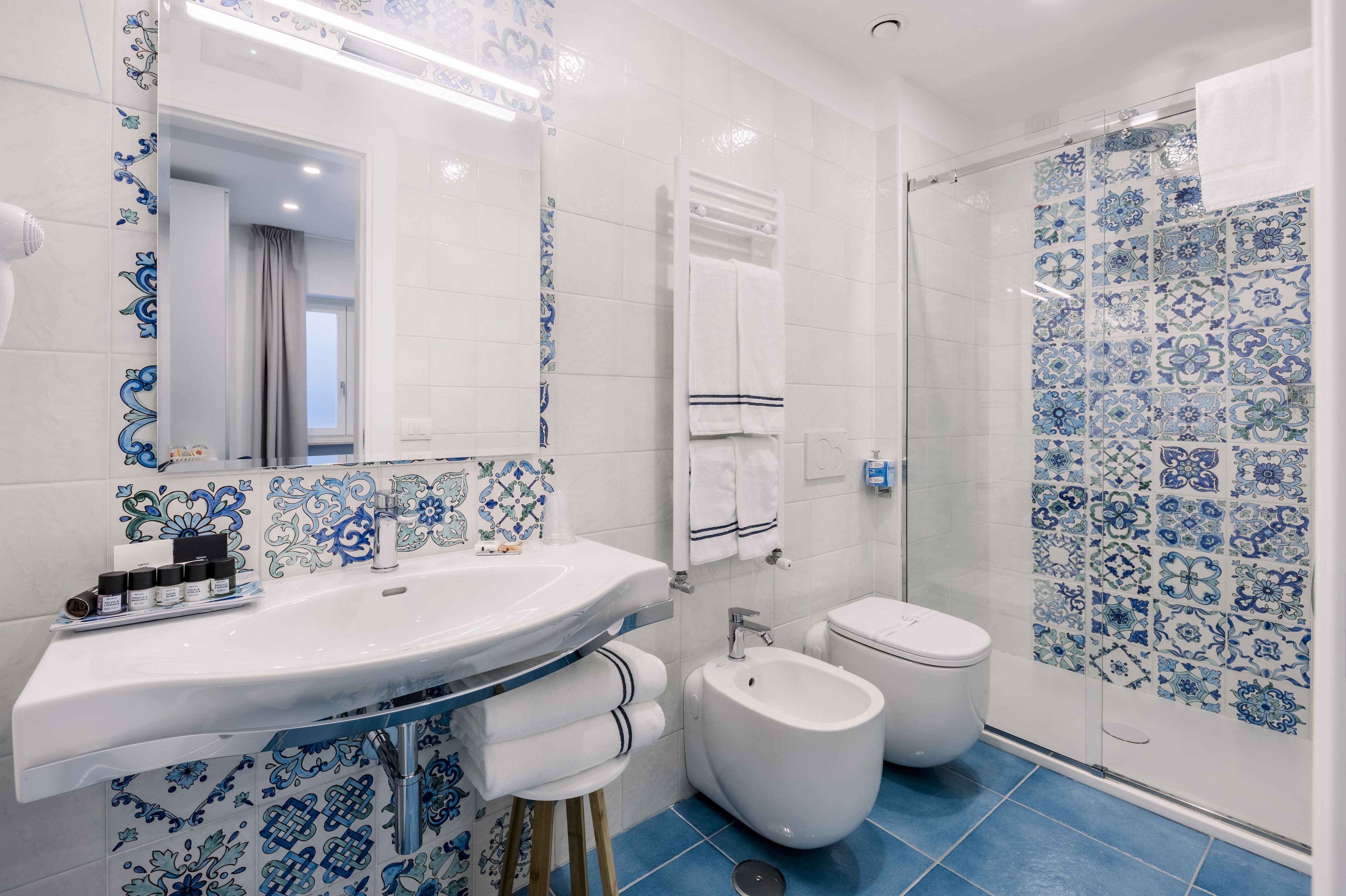 Une salle de bain avec un lavabo blanc, un bidet et des toilettes, dont le sol et les murs sont recouverts de carreaux aux motifs bleus et blancs.