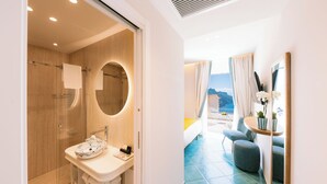 Un baño moderno con cabina de ducha de vidrio, un espejo redondo y un lavamanos blanco con un cuenco decorativo.