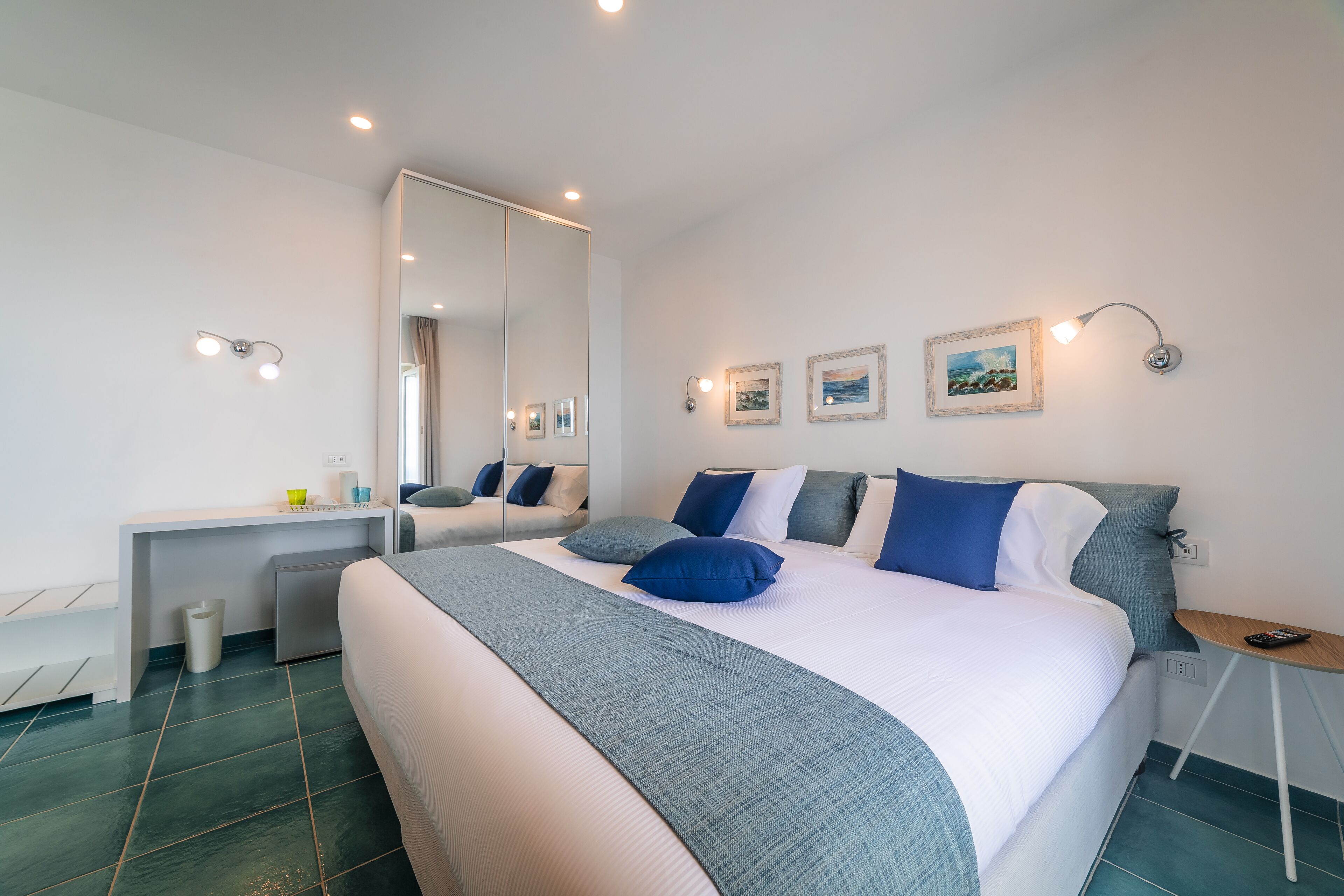 A modern bedroom with a large bed, bedside tables, a desk, and a mirror.