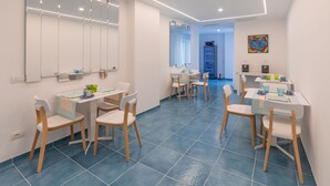 Un comedor moderno con mesas y sillas blancas, piso de baldosas azules y un espejo grande en la pared.