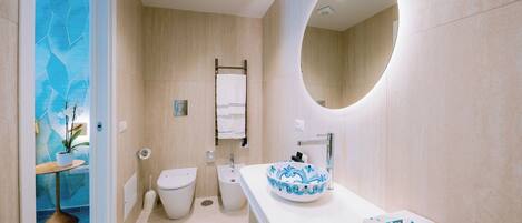 Un baño moderno con inodoro, bidé, lavamanos con un recipiente decorativo y espejo.