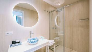 A modern bathroom with a round mirror, a glass-enclosed shower, and a white vanity with a bowl sink.