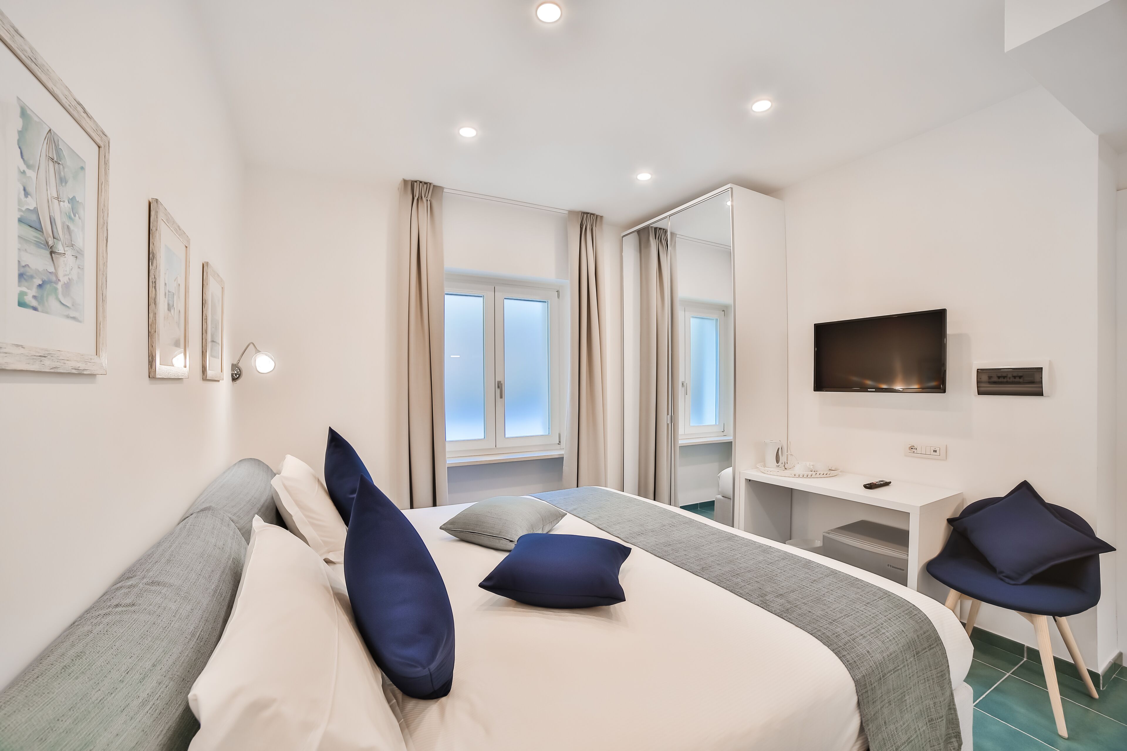 A modern hotel room with a bed, a desk, a TV, and a window with curtains.