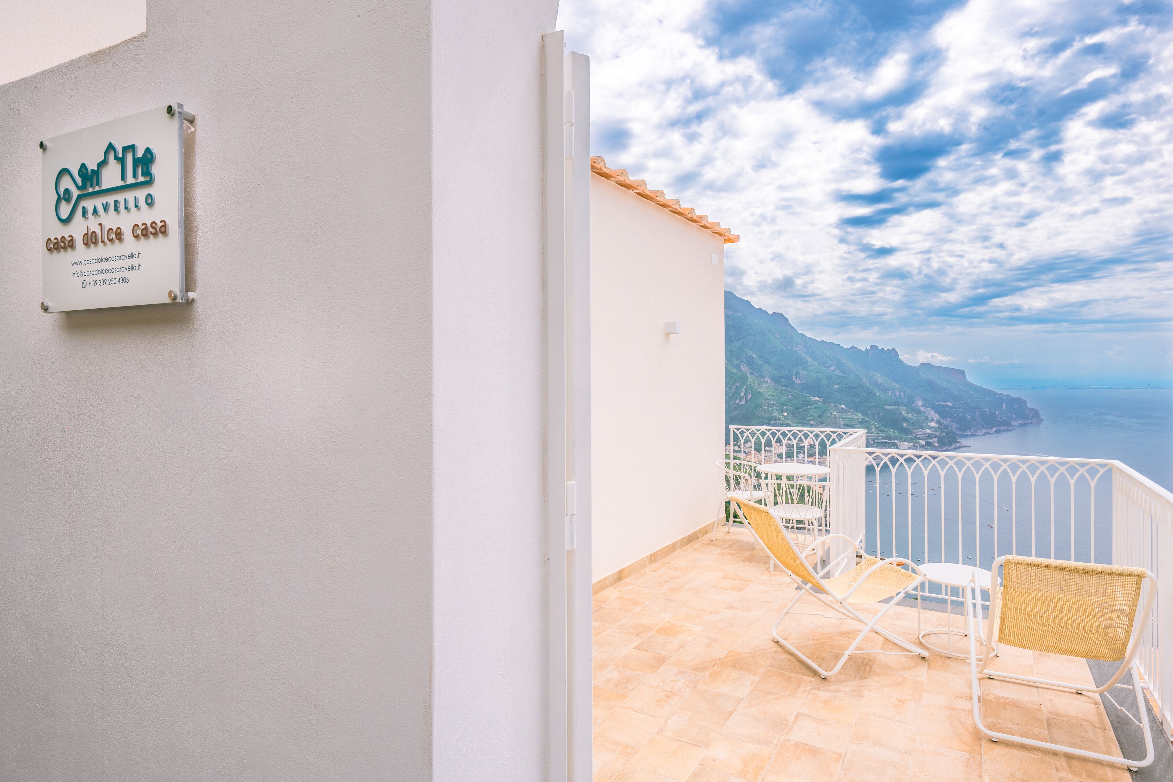 A balcony with a view of the sea and mountains, a signboard, and two chairs.