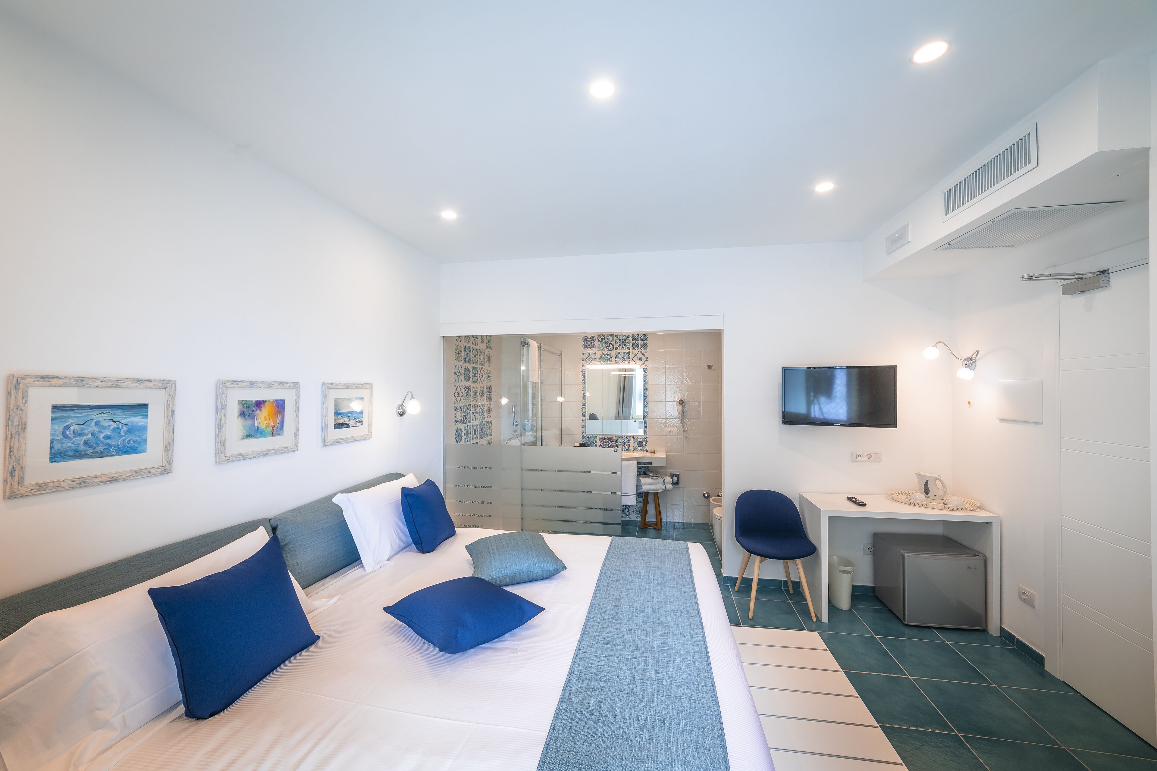 A modern hotel room with a large bed, a desk, a chair, and a TV.