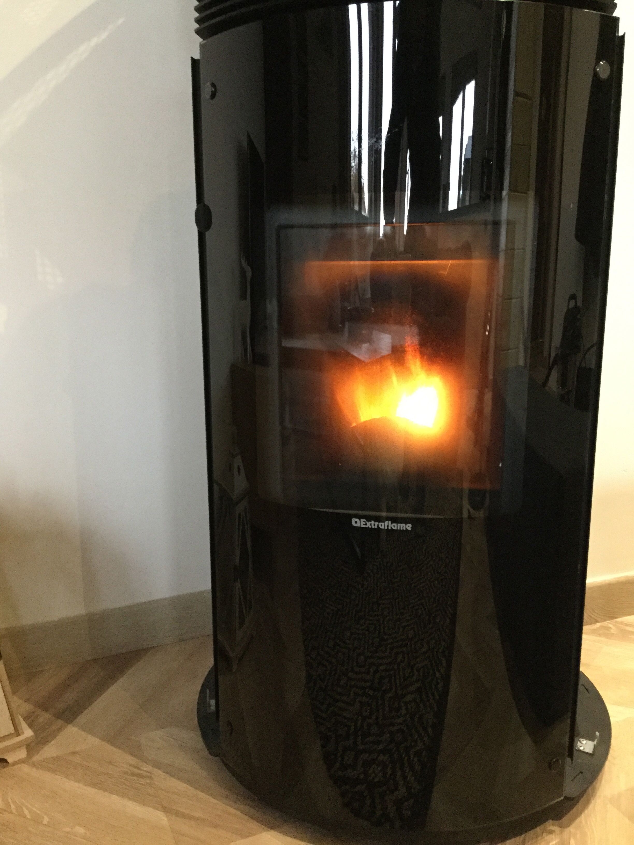 Calentador de vidrio negro con llama visible, etiquetado como "Extraflame", sobre un piso de madera.