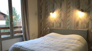 A neatly made bed with a headboard, a window with curtains, and a wall with a geometric pattern. - New! Superb apartment of 90 m2 in the heart of Font Romeu (Font-Romeu-Odeillo-Via)