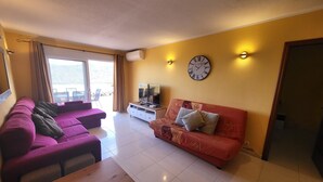 Un salon avec un canapé, un téléviseur, une table en bois et une horloge au mur.