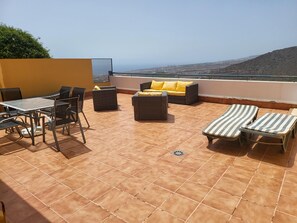 A terrace with a table and chairs, a sofa with yellow cushions, and striped lounge chairs. - Roque Del Conde (Costa Adeje)